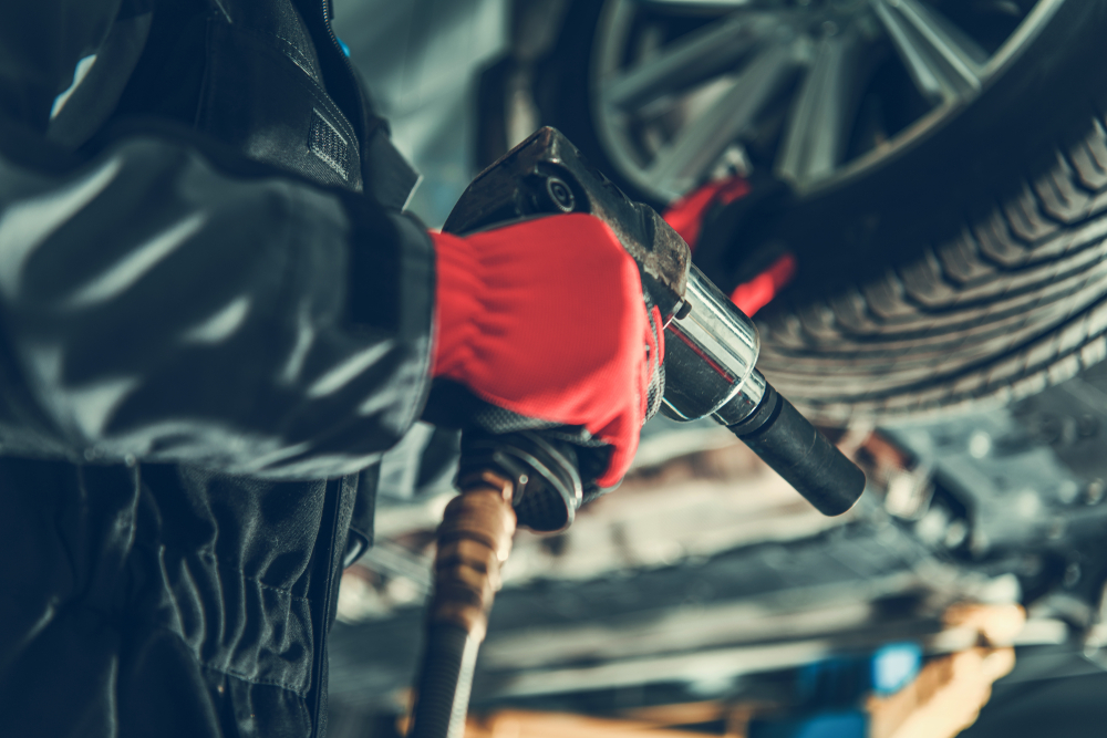 A mechanic using a power tool to rotate a tire on a vehicle.